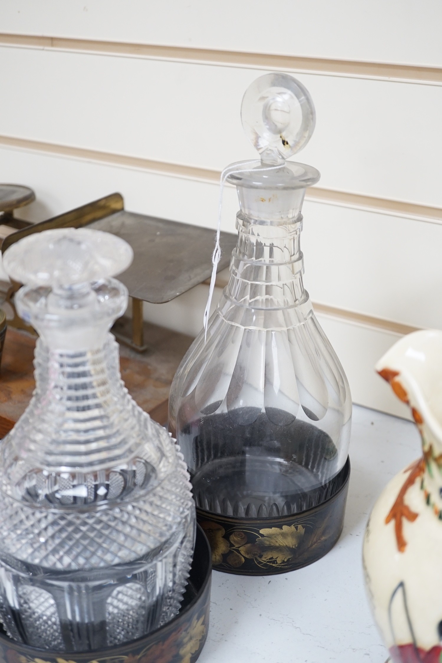 Two Regency cut glass decanters and stoppers and a pair of papier maché wine coasters, tallest 30 cm